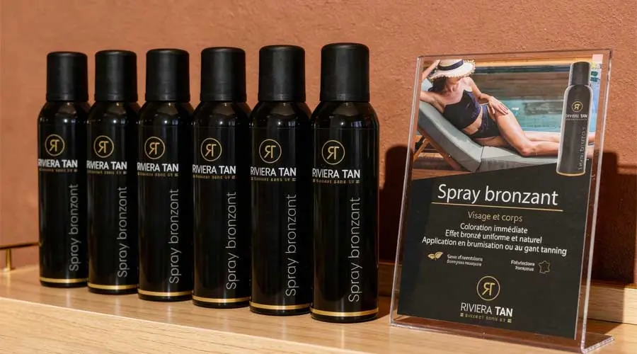 Lot de sprays bronzants Riviera Tan et flyers publicitaires exposés en zone de revente de soins dans un institut de beauté